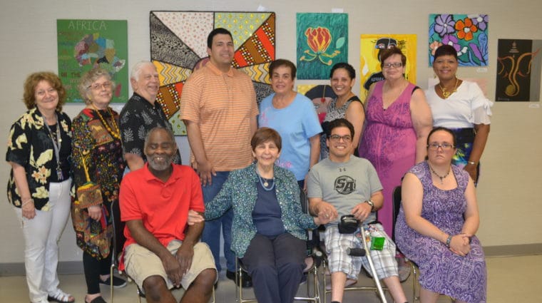 A group of artists from AHRC Nassau's East Meadow Art Gallery pose in front of their art at a local library.