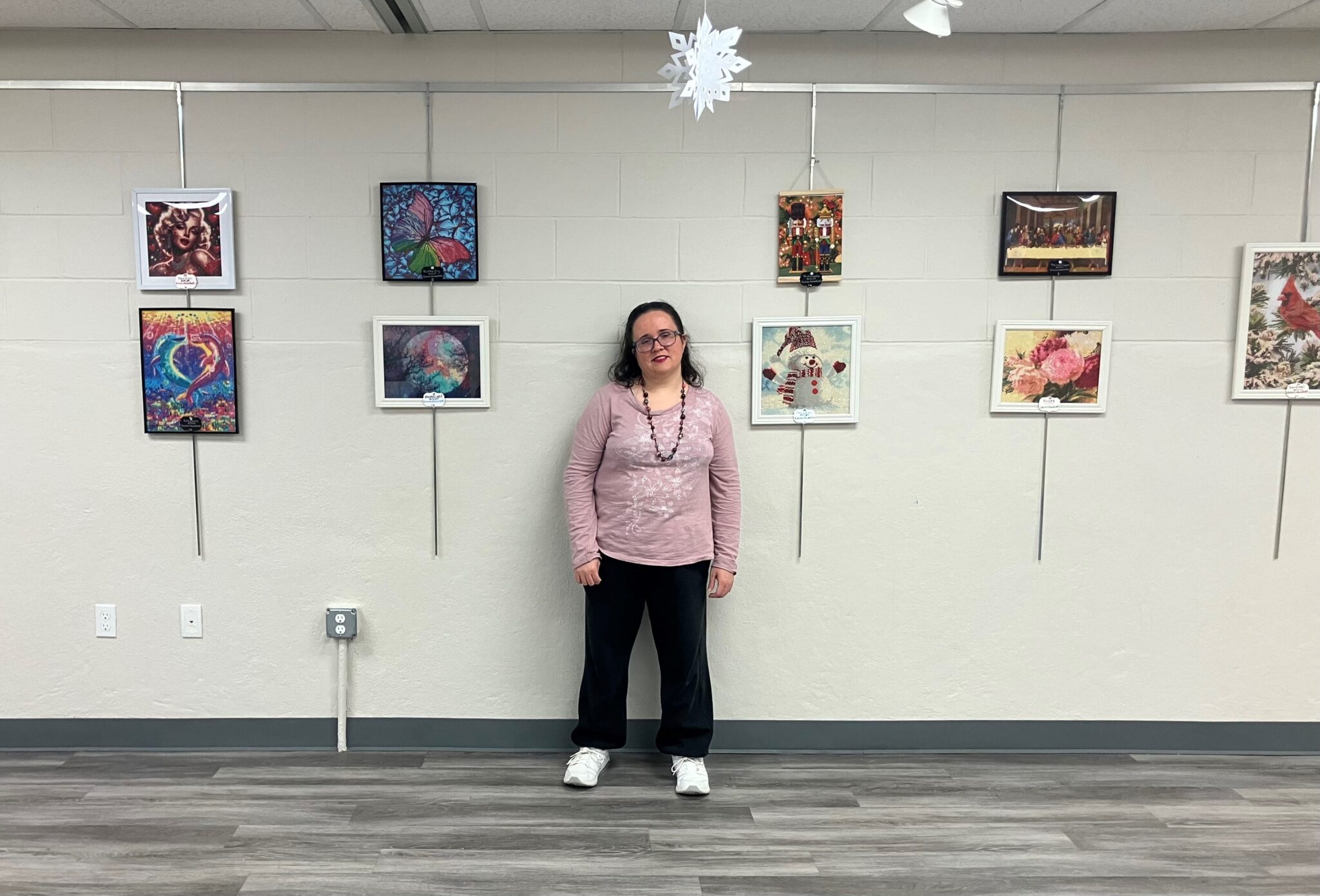 Donna Nowakoski poses in front of a wall of her art