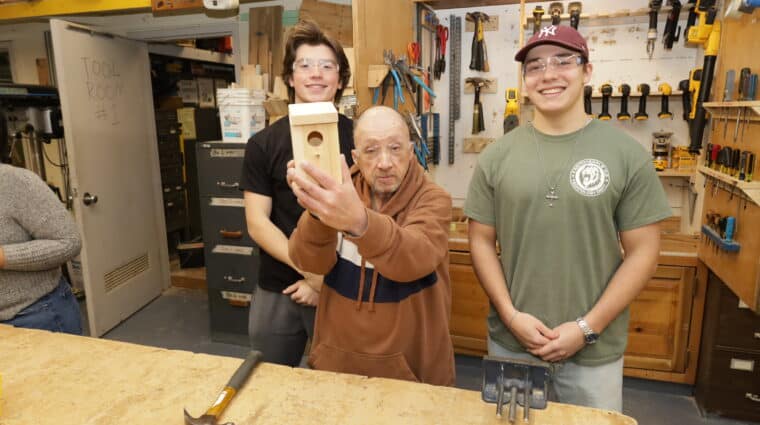 Two Farmingdale High School students pose with a person supported by AHRC Nassau Day Services and the birdhouse he created.