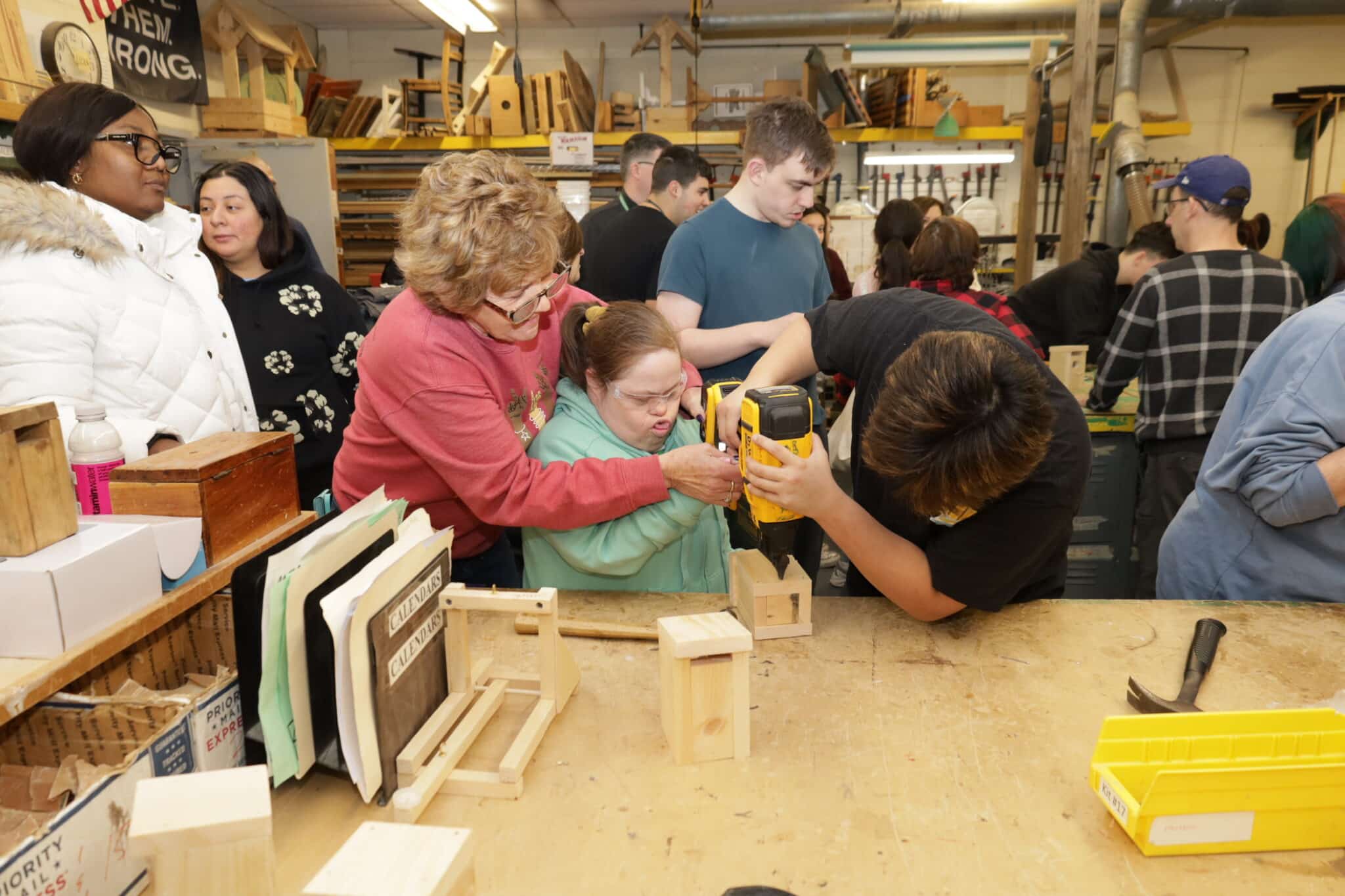 A Farmingdale High School student and teacher help a person supported by AHRC Nassau Day Services drill a hole in her birdhouse.