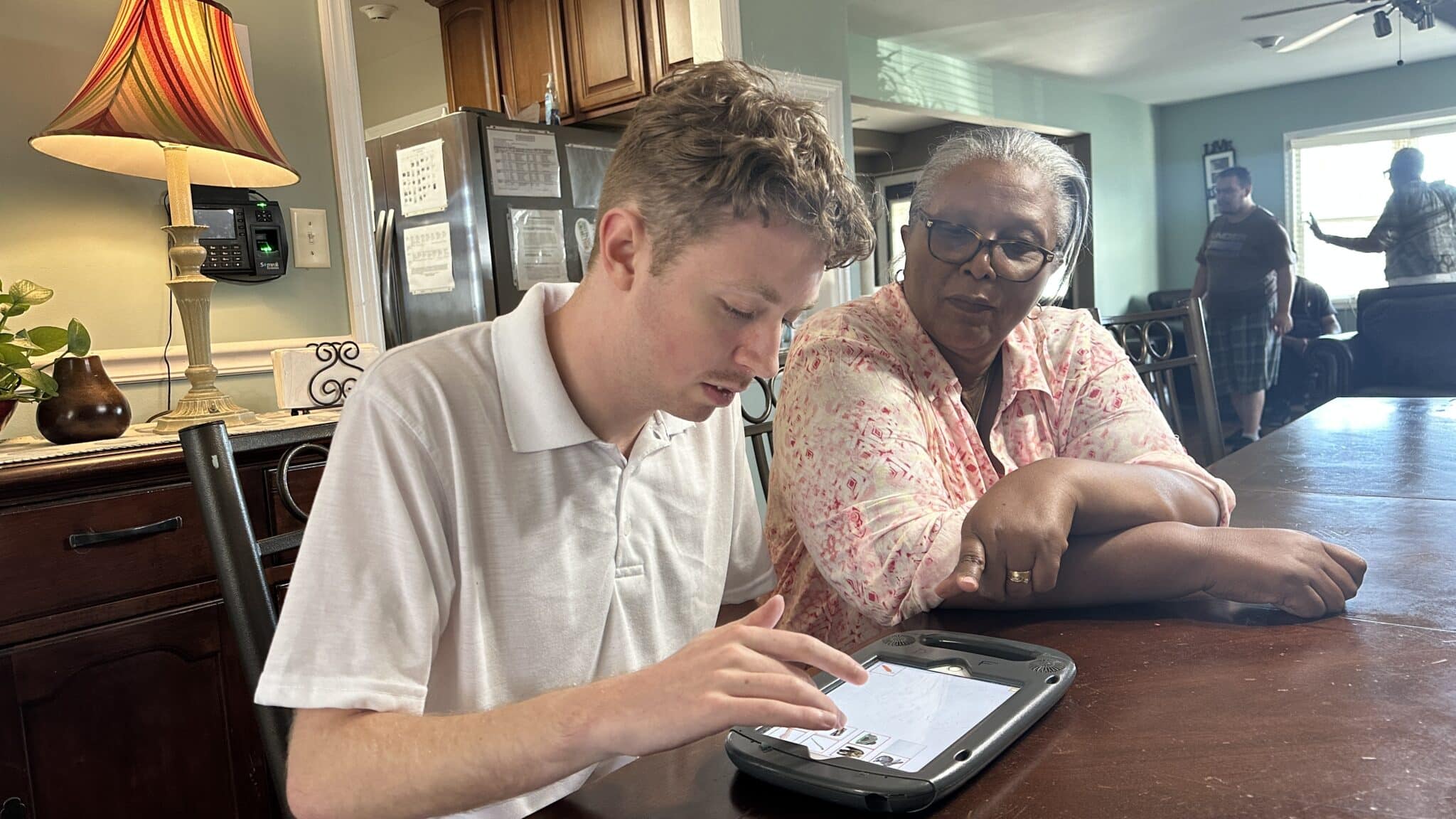 A staff member helps a person supported use his tablet