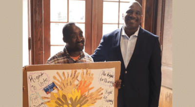 A person supported by AHRC Nassau holds a handmade sign next to CEO Stanfort Perry.