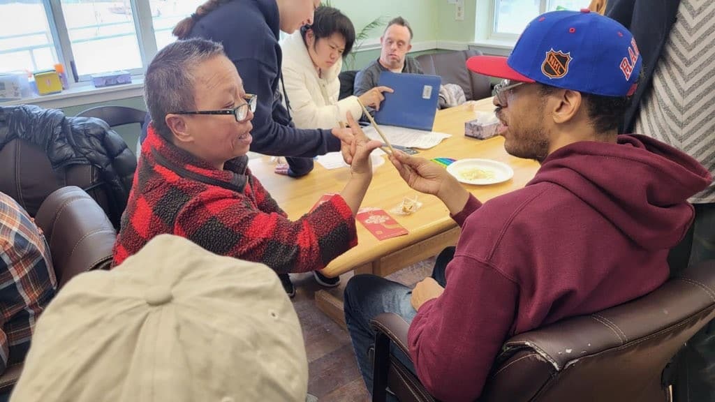 Two people supported with Day Services practice using chopsticks for Lunar New Year.