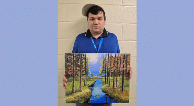 Wenceslao Herrera holds up his painting of trees with a river running through them.