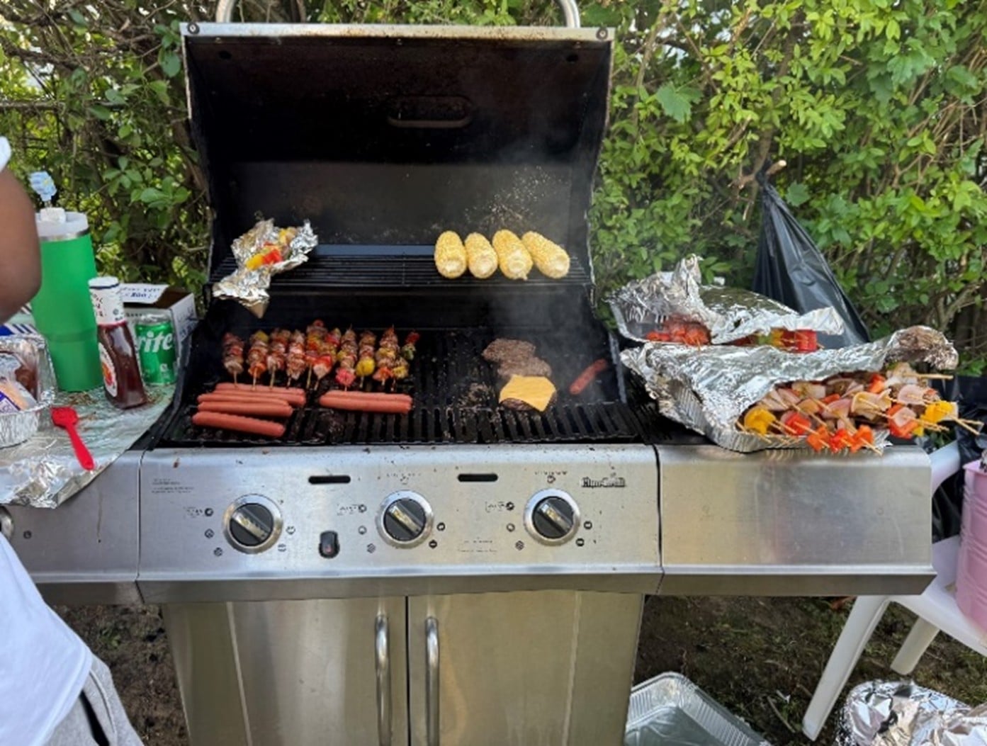 Hot dogs, burgers, corn, skewers and other food on the grill at the summer barbecue.