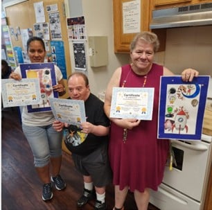 Three people supported by AHRC Nassau and members of the Hooked on Books reading club show off their art and their certificates.