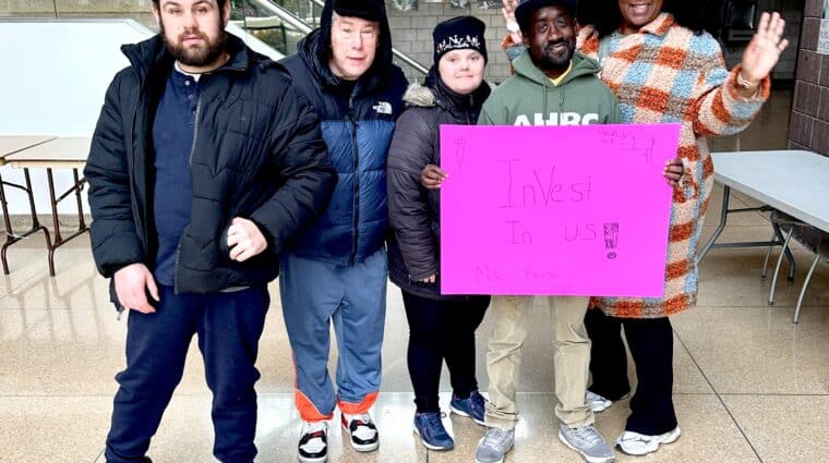 Self-advocates at the rally holding a pink sign reading "Invest in us!"