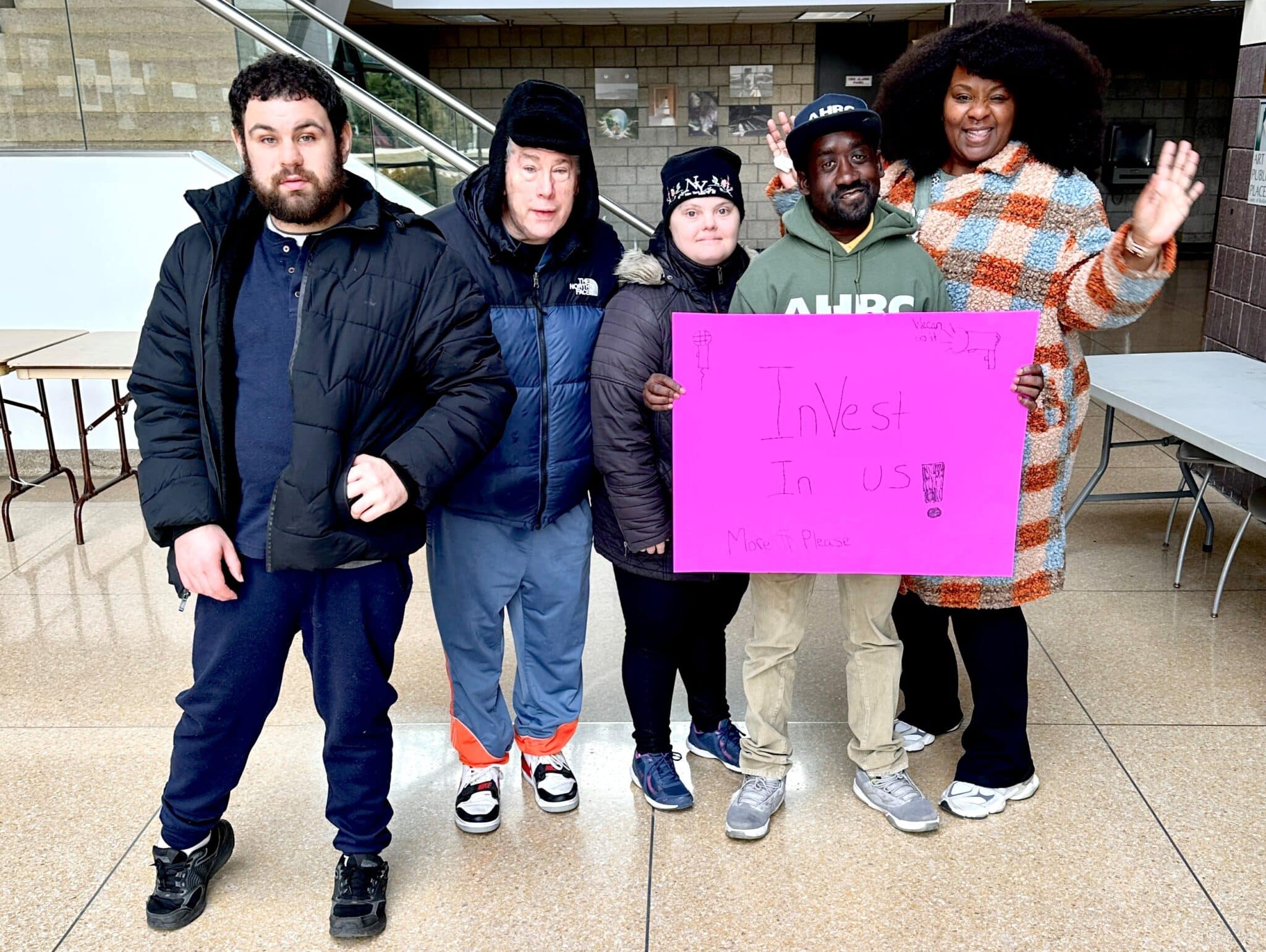 Self-advocates at the rally holding a pink sign reading "Invest in us!"