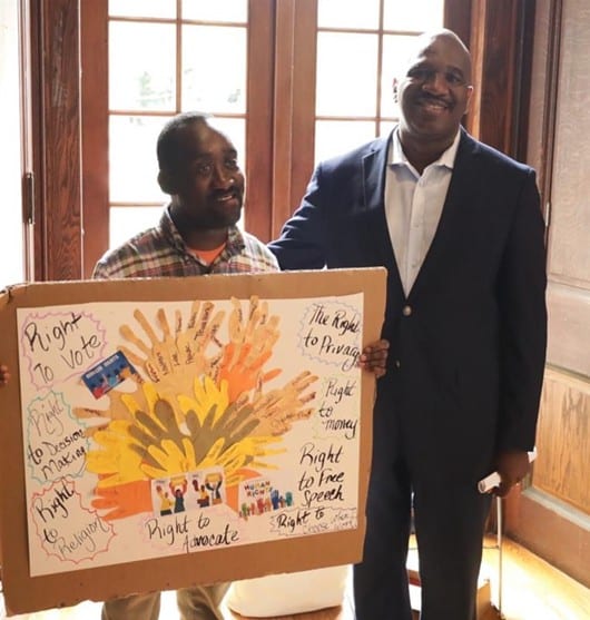 A person supported by AHRC Nassau holds a handmade sign next to CEO Stanfort Perry at the Rights Rally.