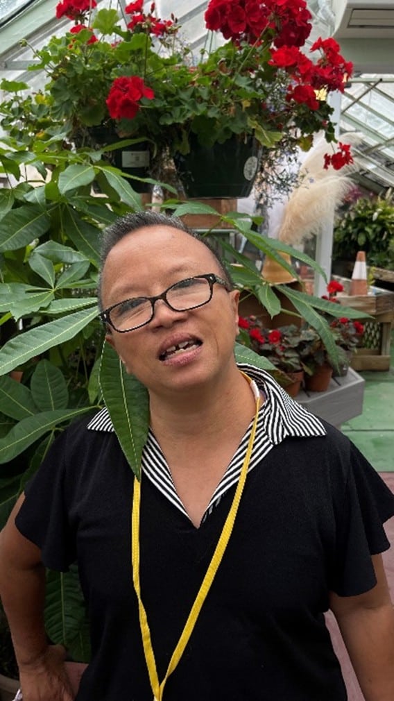 Tracey Zhang in front of green plants and red flowers at her job Wheatley Farms