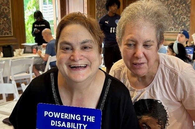 Self-advocates pose with a sign that reads "Powering the disability" at the Voter Demonstration rally
